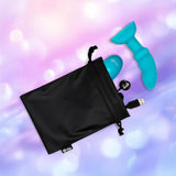 The B-Vibe Remote Rimming P-Spot Plug, a turquoise silicone adult toy by B-Vibe, with remote, USB charging cable, and a Vibe-logo black bag, displayed on a soft purple and blue blurred background. The B-Vibe Remote Rimming P-Spot Plug, a turquoise silicone adult toy by B-Vibe, with remote, USB charging cable, and a Vibe-logo black bag, displayed on a soft purple and blue blurred background.