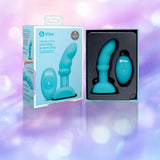 The b-Vibe Remote Rimming P-Spot Plug and its remote are shown in an open B-Vibe box against a purple and light blue blurred background. The b-Vibe Remote Rimming P-Spot Plug and its remote are shown in an open B-Vibe box against a purple and light blue blurred background.