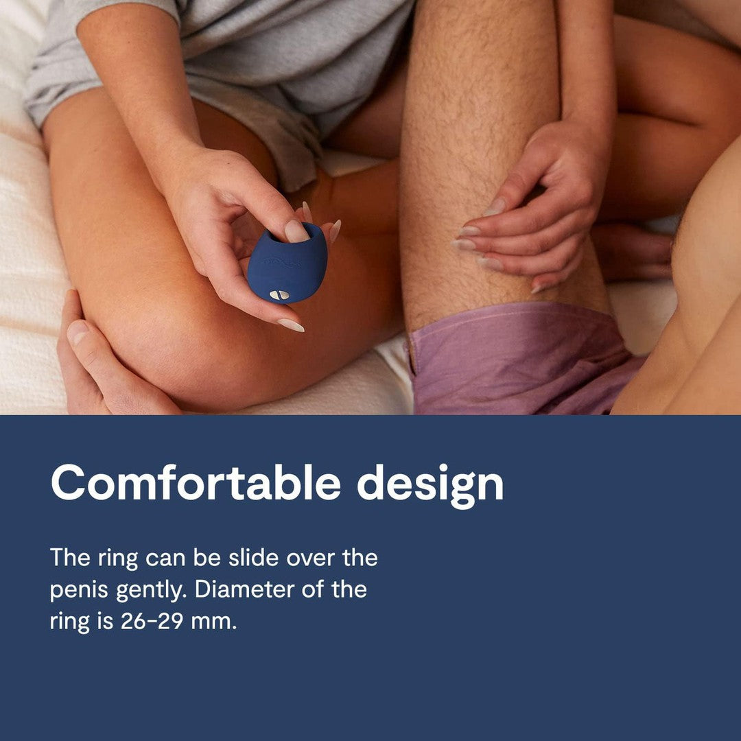 A person holds the compact We-Vibe "Pivot" Vibrating Penis Ring with Smart App beside another individual wearing pink shorts, sitting closely together on a bed. The text reads, "Comfortable design. The We-Vibe 'Pivot' penis ring can be gently slid over the penis. Diameter of the ring is 26-29 mm.