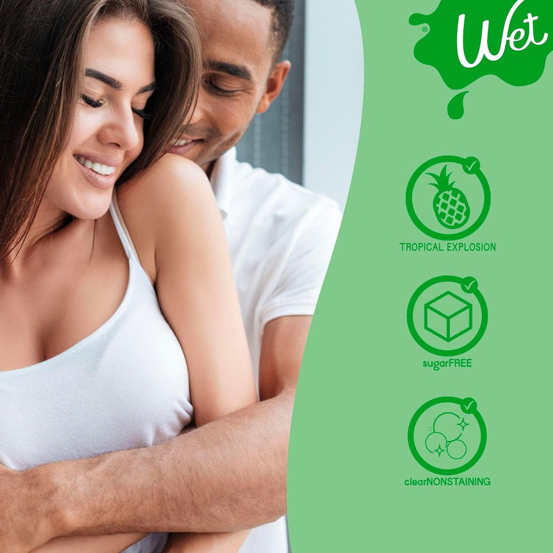 A smiling woman in a white tank top is hugged from behind by a man in a white shirt. To the right, there are product benefits listed: "Wet Tropical Explosion Flavored Lubricant 🍍," "sugarFREE," "clearNONSTAINING," and "water-based formula" with corresponding icons. The brand name "Wet" is prominently displayed at the top right.