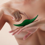 A close-up of a person with bare skin holding a FemmeFunn Unda Panty Vibrator Dark Green in their hands. The person's hands and the vibrator by Femme Funn are centrally framed, set against a light, neutral background.