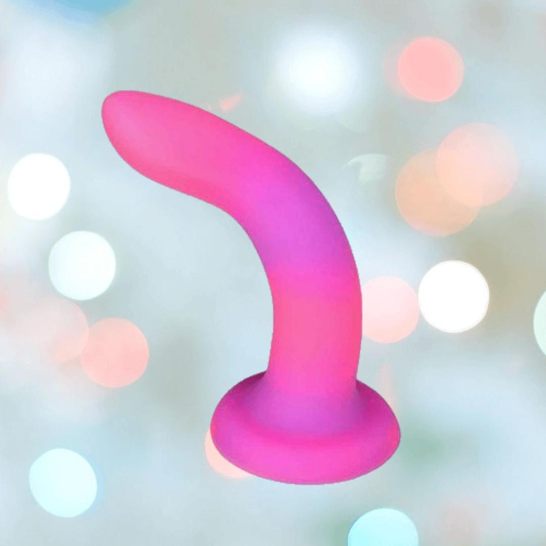 The BMS Addiction Rave Glow-in-the-Dark Bendable Vibrating Dong—Pink Purple 8"—features premium silicone, a curved smooth shape, flared suction base, and is harness compatible, set against a pastel bokeh background.