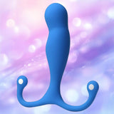 The Aneros Maximus Syn Trident Series Special Edition is a blue silicone prostate massager with two rounded arms, shown against a soft pastel purple and pink bokeh background.