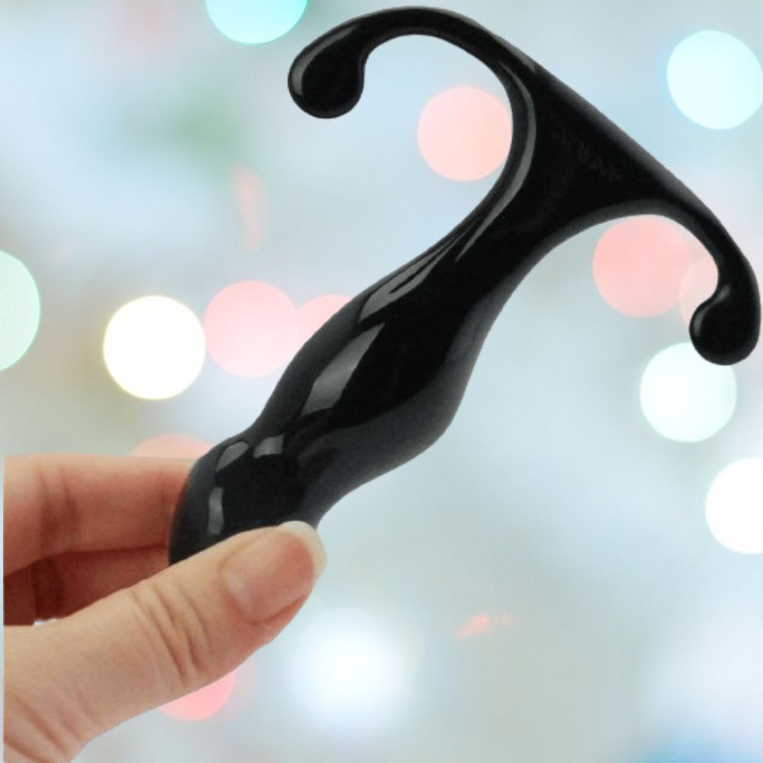 A hand holds a sleek, black tool, probably an Aneros Progasm Jr. Prostate Massager by Aneros, against a blurred background accented with colorful bokeh lighting.