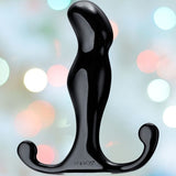 A black, sculpted object with a curved, ergonomic design and two rounded ends looks like the Aneros Progasm Jr. Prostate Massager from Aneros, set against a colorful, blurred background with circular light spots.