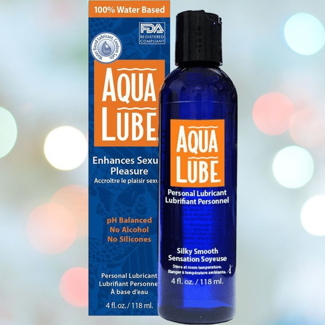 Image of a product called "Aqua Lube Water-Based Personal Lubricant" from the brand Aqua Lube by Kimono, featuring a prominent blue bottle with an orange label. The packaging indicates it is a 100% water-based personal lubricant that enhances sexual pleasure, is pH balanced, free from alcohol and silicones, and offers a silky smooth sensation.