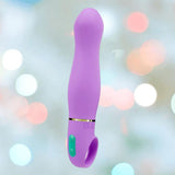 The Aria Rechargeable Vibe Exciting AF-Indigo by Blush Novelties is a purple silicone vibrator with a curved design and green control buttons, shown against a soft, pastel-lit background.