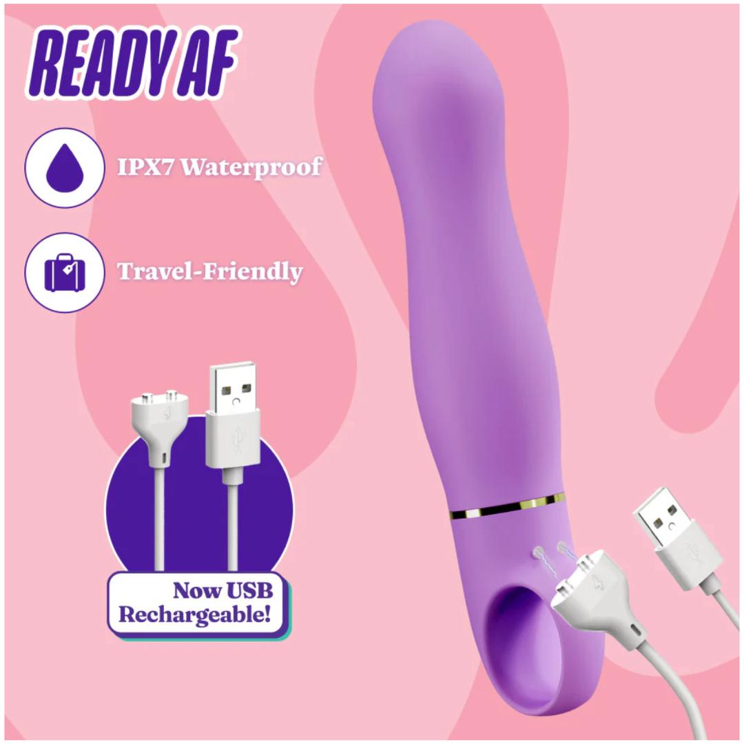 The Blush Novelties Aria Rechargeable Vibe Exciting AF-Indigo, a purple silicone G-spot vibrator with a curved design, is IPX7 waterproof, travel-friendly, and USB rechargeable. A USB charging cable is shown beside it on a pink background.