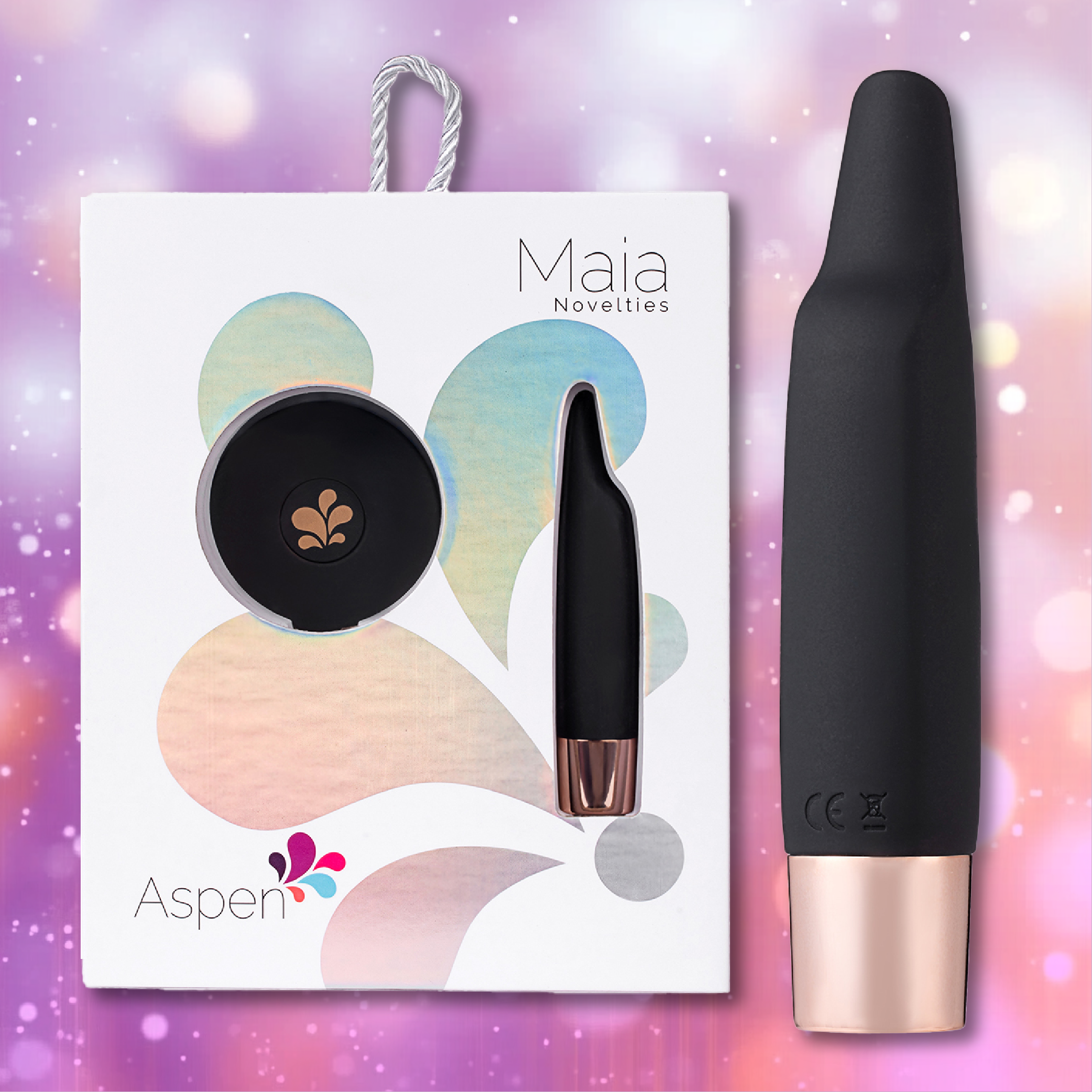 A black and rose gold personal massager, the Aspen 15-Function Flickering Tip Vibrator by Maia Toys, known as a compact pleasure companion, is displayed in its packaging labeled "Maia Toys Aspen" against a blurred, colorful background with light bokeh effects.