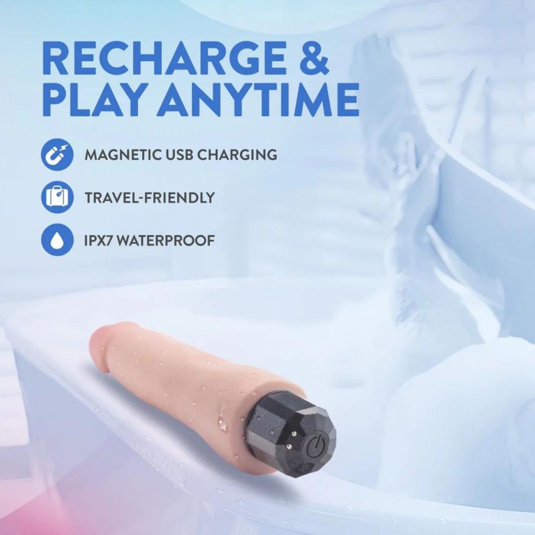 The Au Naturel Vanilla Ice Vibrating Dildo by Blush Novelties, shown with water droplets on a bathtub edge, features magnetic USB charging, is travel-friendly and IPX7 waterproof—perfect for recharge & play anytime. A blurred bathroom scene completes the setting.