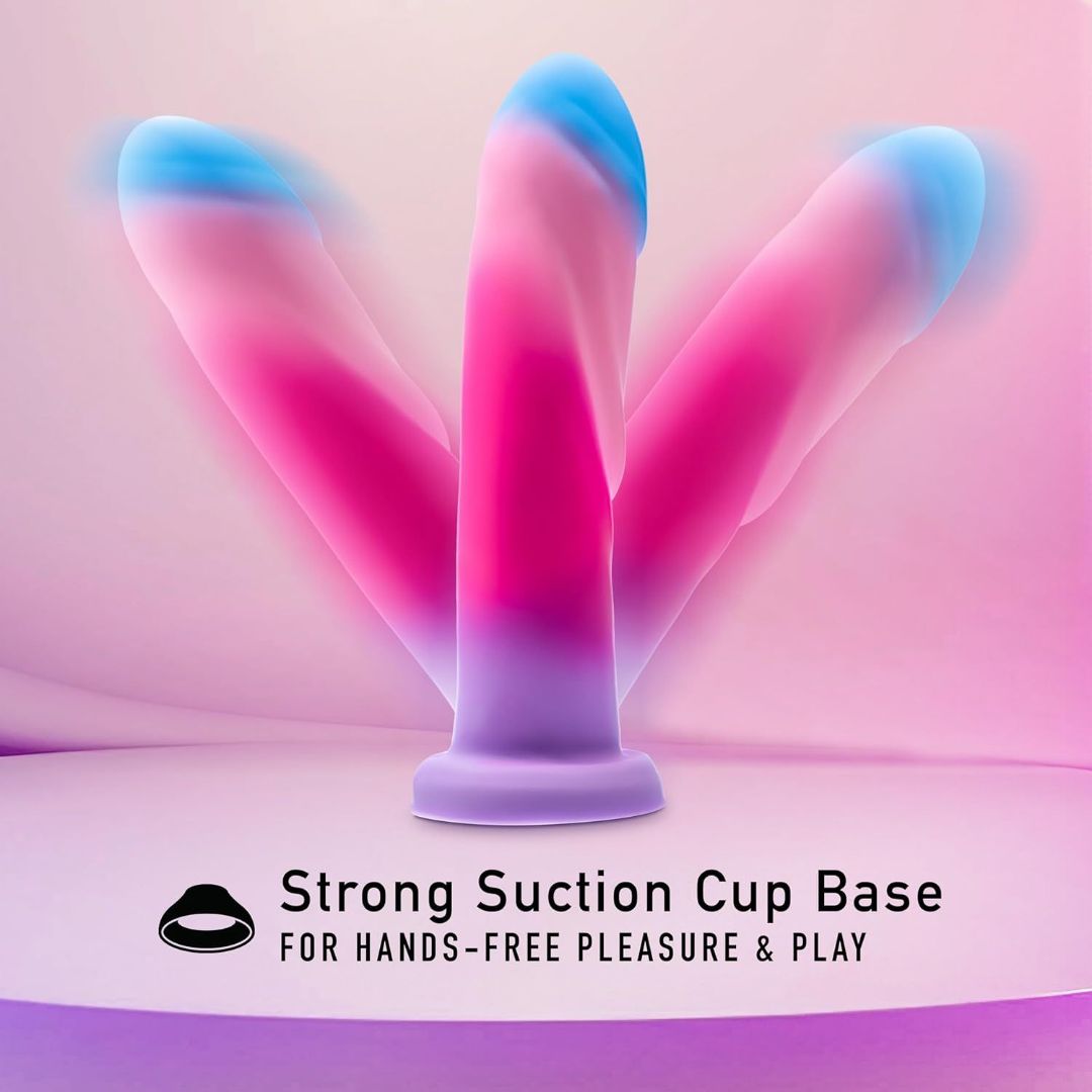 Displayed against a pink and purple gradient background is the Avant Borealis Dreams - Cotton Candy Realistic Dildo, an artisanal piece by Avant featuring a vibrant color palette. The text highlights its "Strong Suction Cup Base for Hands-Free Pleasure & Play." Crafted from platinum-cured silicone, this dildo is also harness compatible for versatile enjoyment.