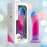 The packaging of the Avant Borealis Dreams - Cotton Candy Realistic Dildo displays a vibrant swirl of pink, purple, and blue. It highlights a hand-sculpted design crafted from platinum-cured silicone and features a strong suction base set against a blurred pastel backdrop. Additionally, it's compatible with harnesses for versatile use.