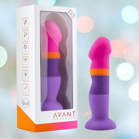 The Avant D3 7" Non-Porous Silicone Dildo - Summer Fling, featuring vibrant shades of pink, orange, and purple with a suction cup base, is showcased alongside its packaging. The box highlights the product's features and displays the brand name "Avant." A soft background with blurred lights emphasizes the body-safe design. 1080