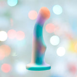 The Avant Opal Dreams Dildo - Aqua by Avant is a pastel-colored silicone sculpture with a smooth, curved shape and flat base, showcased against a softly blurred background with gentle bokeh light effects.