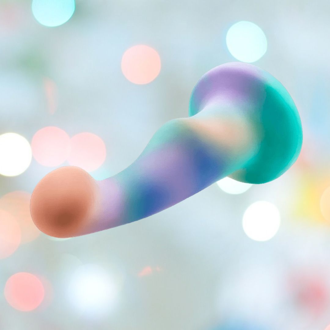 The Avant Opal Dreams Dildo – Aqua by Avant is a silicone dildo with a curved shape for G-spot stimulation and a flared base, featuring a pastel swirl of blue, purple, and green against a soft, bokeh-style background.