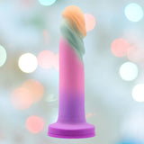 The Avant Sunrise Gaze - Sherbet Realistic Dildo is a vibrant silicone piece showcasing purple, pink, and blue-green hues crafted with platinum-cured silicone. Its gradient design boasts a sturdy suction cup base and is beautifully displayed against a backdrop of pastel-colored bokeh lights.