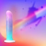 The Avant D17 'Lucky' Non-Porous Silicone Dildo by Avant stands upright in pastel rainbow colors, with a unicorn silhouette and rainbow trail in the blurred, vibrant background.