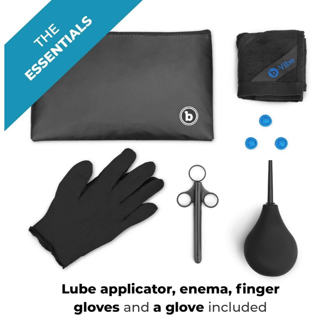 A flat lay shows the B-Vibe Anal Massage & Education Set: black pouch, towel, three blue caps, glove, lube applicator syringe, and enema bulb. Text: “THE ESSENTIALS by B-Vibe. Includes lube applicator, enema bulb, finger gloves & more.”.