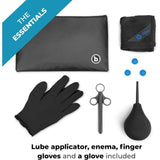 A flat lay shows the B-Vibe Anal Massage & Education Set: black pouch, towel, three blue caps, glove, lube applicator syringe, and enema bulb. Text: “THE ESSENTIALS by B-Vibe. Includes lube applicator, enema bulb, finger gloves & more.”.