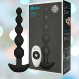 The B-Vibe Cinco Beads XL Vibrating Anal Beads in black, its remote control, and the branded packaging are shown against a softly blurred pastel background.