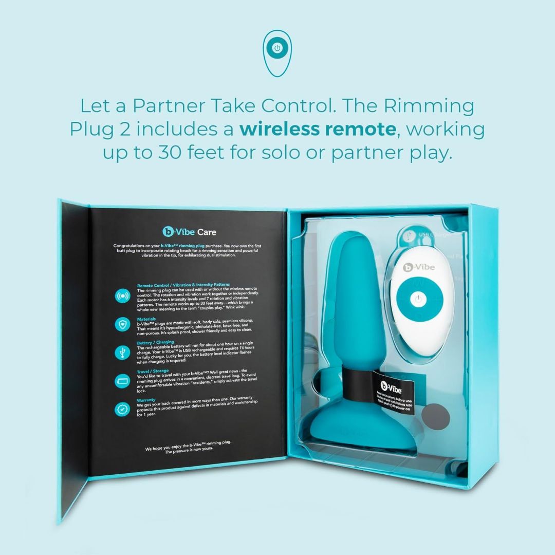 A blue and white B-Vibe box contains a black and blue silicone B-Vibe Rimming Plug 2 Vibrating Butt Plug and a white wireless remote. The lid highlights partner play, vibration features, and product details in blue and white text.