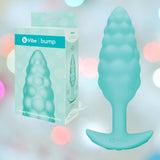The B-Vibe Texture Vibrating Butt Plug Bump (Small, Mint) sits by its box. Made from body-safe silicone with a flared base for comfort and safety, it’s perfect for playful anal fun. Pastel bokeh lights add a whimsical touch to the scene.