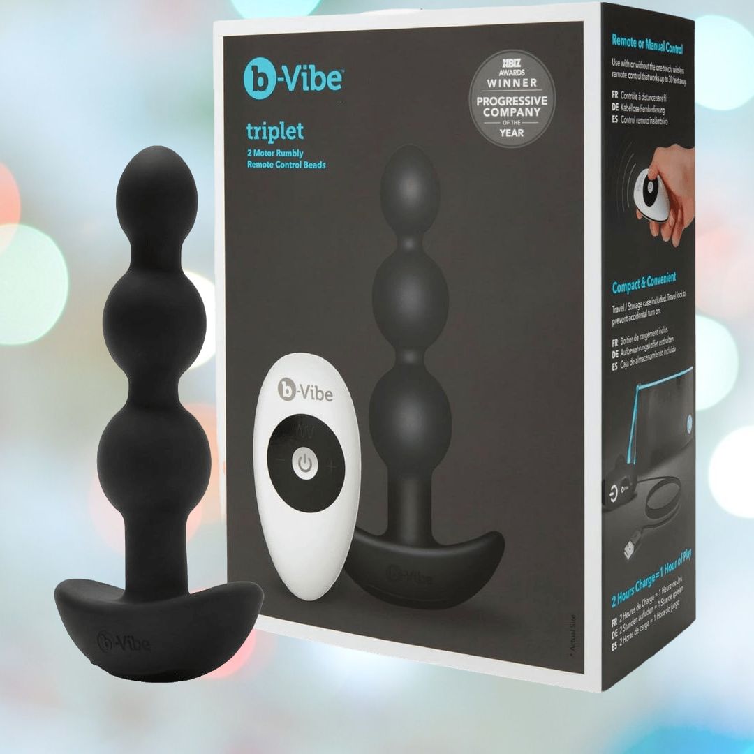 The B-Vibe Triplet Beads Vibrating Anal Beads - Black, a white remote control, and branded b-Vibe packaging are shown on a pastel background. The box highlights the wireless remote and compact silicone design.