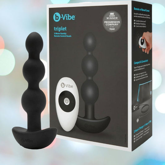 The B-Vibe Triplet Beads Vibrating Anal Beads - Black, a white remote control, and branded b-Vibe packaging are shown on a pastel background. The box highlights the wireless remote and compact silicone design. 1080