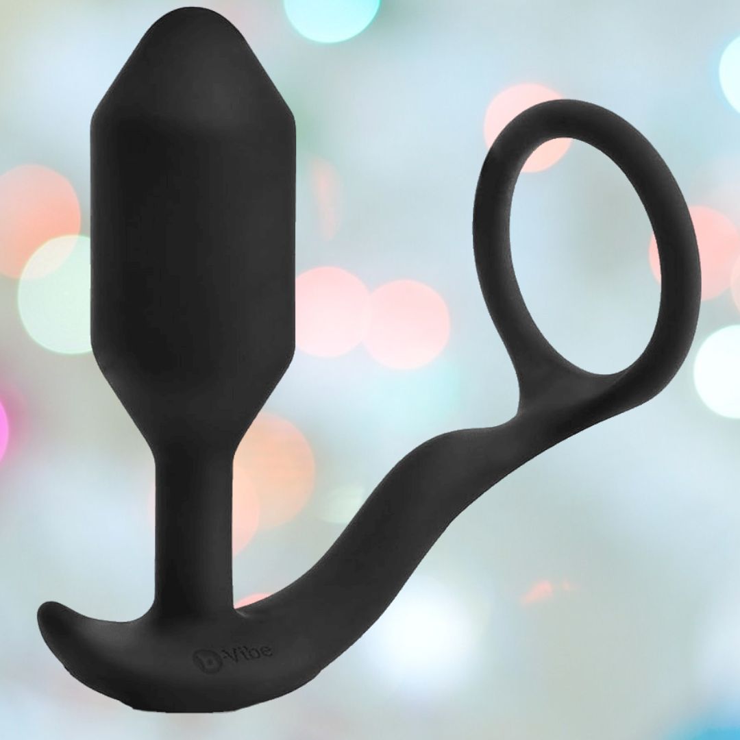 The B-Vibe Vibrating Cock Ring - Snug & Tug (M) by B-Vibe, featuring a curved base and circular ring handle, is displayed against a softly blurred, colorful background.