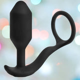The B-Vibe Vibrating Cock Ring - Snug & Tug (M) by B-Vibe, featuring a curved base and circular ring handle, is displayed against a softly blurred, colorful background.