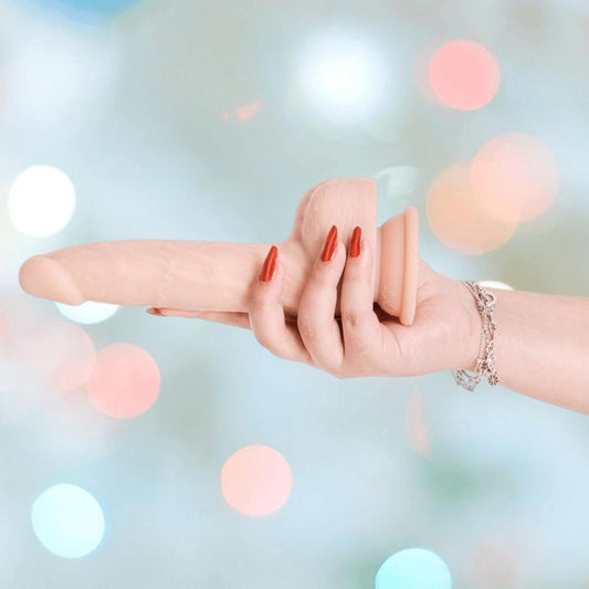 A hand with red-painted nails and a silver bracelet holds the BMS Naked Addiction Thursting Dong - Vanilla 8.5" against a blurred background of pastel-colored lights. 1080