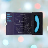 The BMS The Mini Swan Wand Glow in the Dark - Blue is shown in an open black box that reads "GET READY TO GLOW." on the lid, with white outlines and instructions. The blurred background has colorful lights.