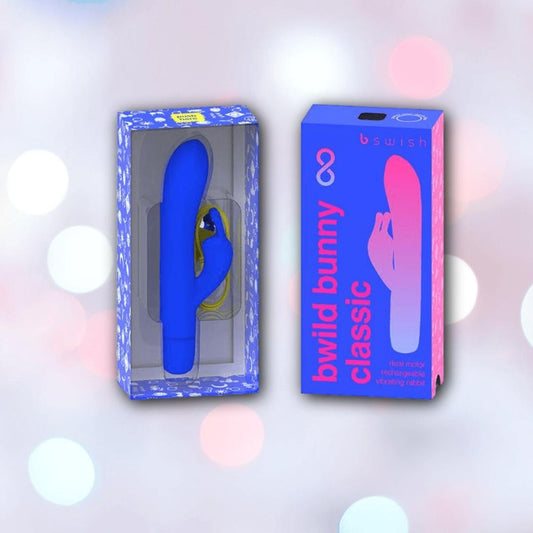 The B Swish Bwild Classic Infinite Bunny - Pacific Blue from Condomania.com is shown in clear packaging beside its box, standing out against a pastel background with pink and blue accents. The waterproof silicone rabbit vibrator features a striking blue color. 1080