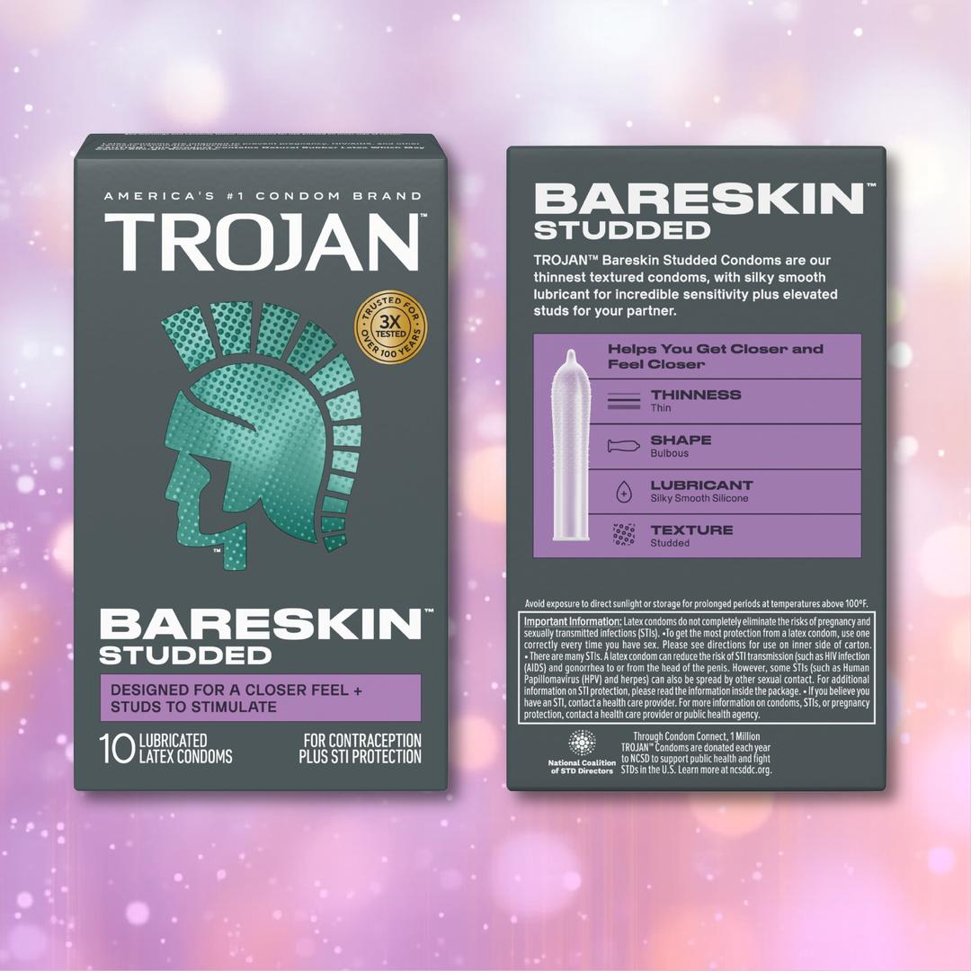 Two boxes of Trojan Studded Bareskin Condoms by Trojan are shown against a pink and purple bokeh background. The front box features the brand logo and product name, while the back box highlights key features of these thin, textured condoms, including their enhanced shape and added lubricant.
