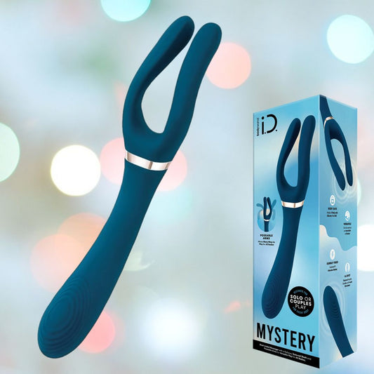 A Bodywand i.D. Mystery Vibrator by XGEN LLC, featuring an innovative forked design in blue, is showcased against a blurred backdrop of multicolored bokeh lights. Next to it lies the packaging adorned with the word "MYSTERY," which mirrors the vivid graphics and detailed product information, assuring delightful G-spot stimulation. 1080