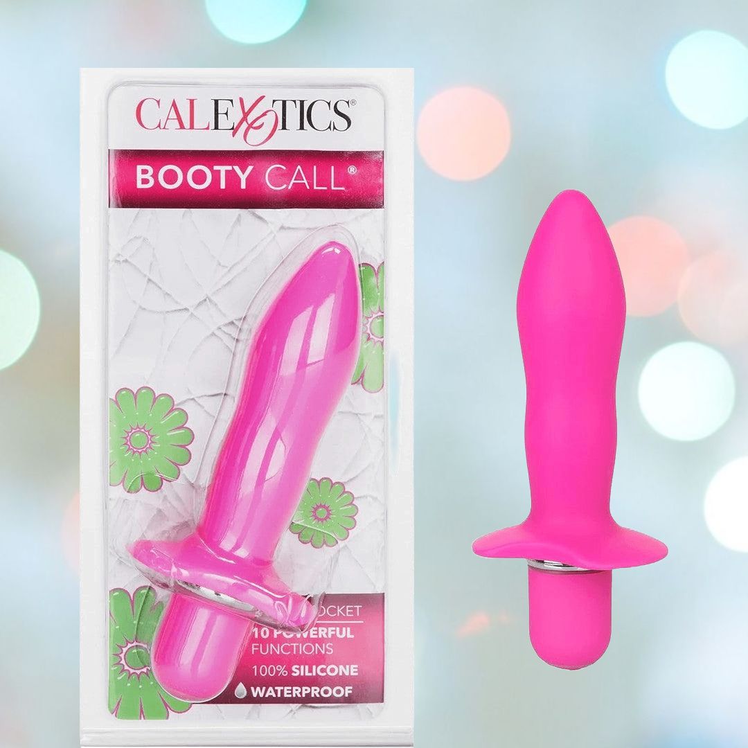 The Booty Call "Booty Rocket" Vibrating Anal Stimulator by CalExotics is displayed alongside its attractive floral-themed packaging. This boxed pink silicone personal massager, specifically designed for prostate stimulation, highlights its waterproof feature and various functions. The image is accentuated by soft focus lights in the background.