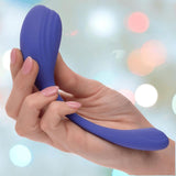 A hand with light pink manicured nails holds the CalExotics Connect Kegel Exerciser, a blue curved silicone device by CalExotics, against a soft, blurred background with colorful lights.
