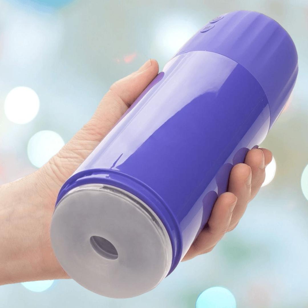 A hand holds the CalExotics Connect Stroker with Vibration and Suction—a purple cylindrical device by CalExotics, featuring a soft gray circular opening—against a blurred background with light spots.