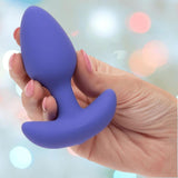 A hand with pink-painted nails holds the CalExotics Connect Tapered Probe App Controlled Anal Vibrator by CalExotics against a soft, blurred background with pastel-colored lights.