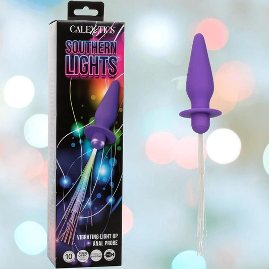 A box labeled "CalExotics Southern Lights Vibrating Light Up Butt Plug Anal Vibrator Probe - Purple" is shown beside a purple silicone butt plug by CalExotics, featuring a flared base and light-up fibers against blurred colorful lights. 1080
