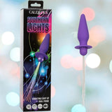 A box labeled "CalExotics Southern Lights Vibrating Light Up Butt Plug Anal Vibrator Probe - Purple" is shown beside a purple silicone butt plug by CalExotics, featuring a flared base and light-up fibers against blurred colorful lights.