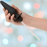 A hand holds the CalExotics Southern Lights Vibrating Light Up Butt Plug Anal Vibrator Probe, featuring clear fiber optic strands extending from its base, against a backdrop of colorful, blurred bokeh lights.