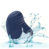 The CalExotics Cashmere Dual Finger Massager, a black, oval-shaped, ribbed device, is shown partially submerged in splashing water against a white background, highlighting its waterproof design.