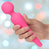 A hand with manicured nails holds the CalExotics Couture Collection Body Wand, a bright pink wand-shaped massager, against a soft pastel bokeh background.
