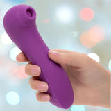 A hand holds the CalExotics Couture Collection Dual Pleasure Wand, a purple silicone massager, against a softly blurred background with pastel-colored lights.