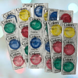 A collection of vibrant, lubricated latex condoms in individual wrappers is arranged in a pile. These Crown Assorted Colors Lubricated Latex Condoms feature shades of red, yellow, blue, and green, with packaging labeled "Colors" and "Crown Assorted." The background softly blurs with bokeh light effects.