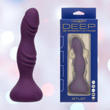 A purple, body-safe silicone probe with a rippled, textured curve stands by its blue and white CalExotics packaging labeled “Deep Stud Reverberating Probe: Rippled Textured Vibrator” against a softly blurred pastel background.