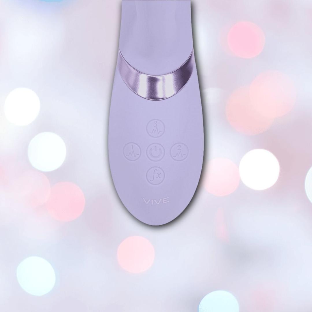 A close-up of the lavender Dolce Vive Fronda Rechargeable G-Spot Vibrating and Tapping Leaf Clit Stim by Shots America, featuring four buttons and the "VIVE" logo, set against a pastel bokeh background of pink, blue, and white lights.