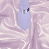 A close-up of the lavender Dolce Vive Fronda Rechargeable G-Spot Vibrating and Tapping Leaf Clit Stim by Shots America, featuring control buttons, rests on shiny light purple satin fabric. The brand name "Shots America" is visible on the device.