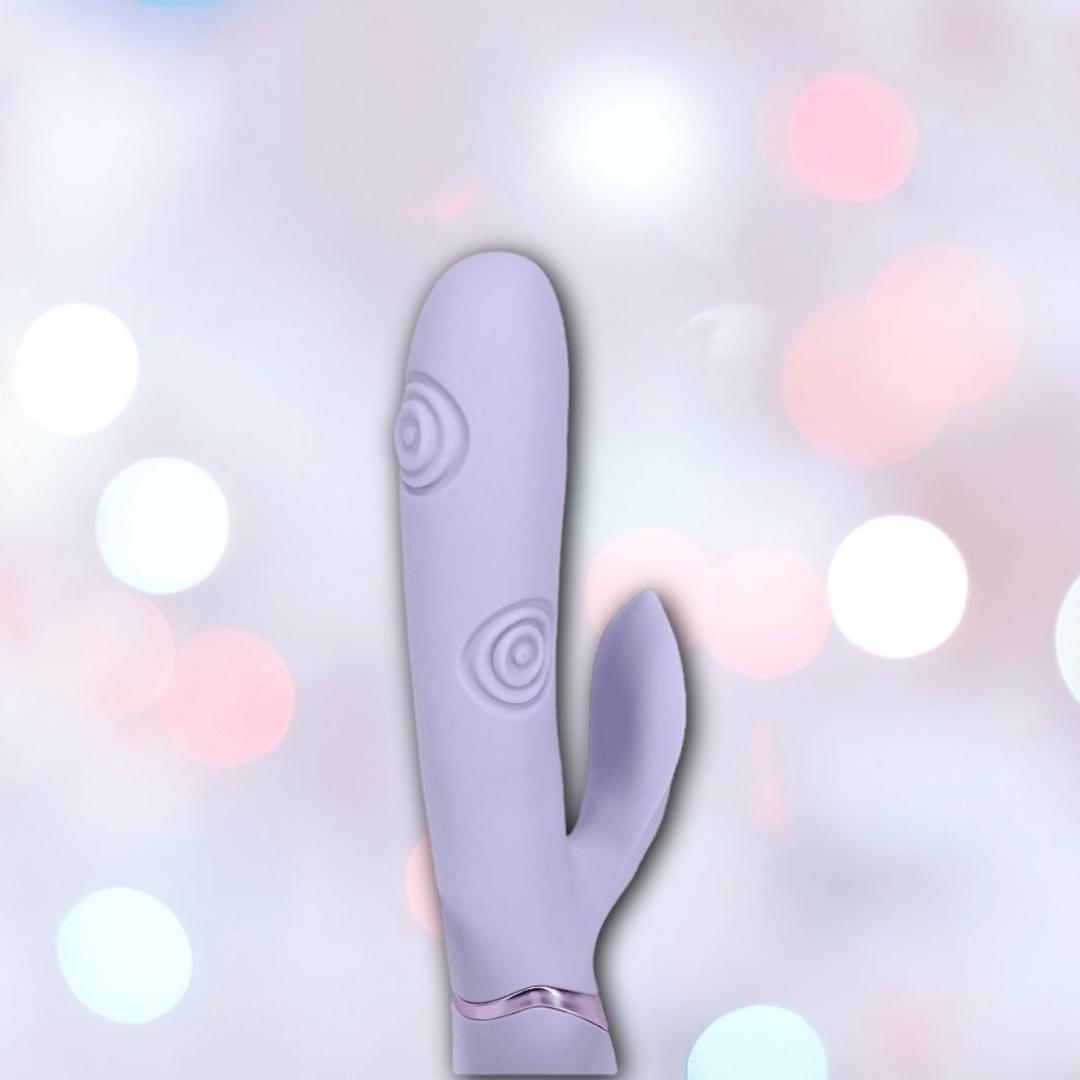 The Dolce Vive Fronda Rechargeable G-Spot Vibrating and Tapping Leaf Clit Stim by Shots America, in lavender, features a curved shaft and leaf-shaped clitoral stimulator, displayed against a soft pastel bokeh background.